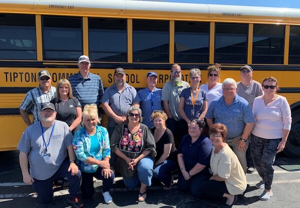 group of bus drivers pictured in front of a yellow school bus