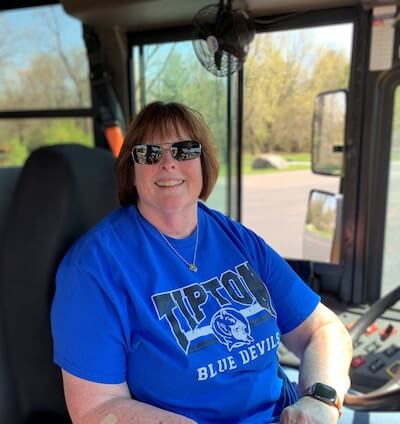 Kelly wears a blue Tipton Blue Devils t-shirt; she has medium-length brown hair and is wearing sunglasses and an Apple Watch