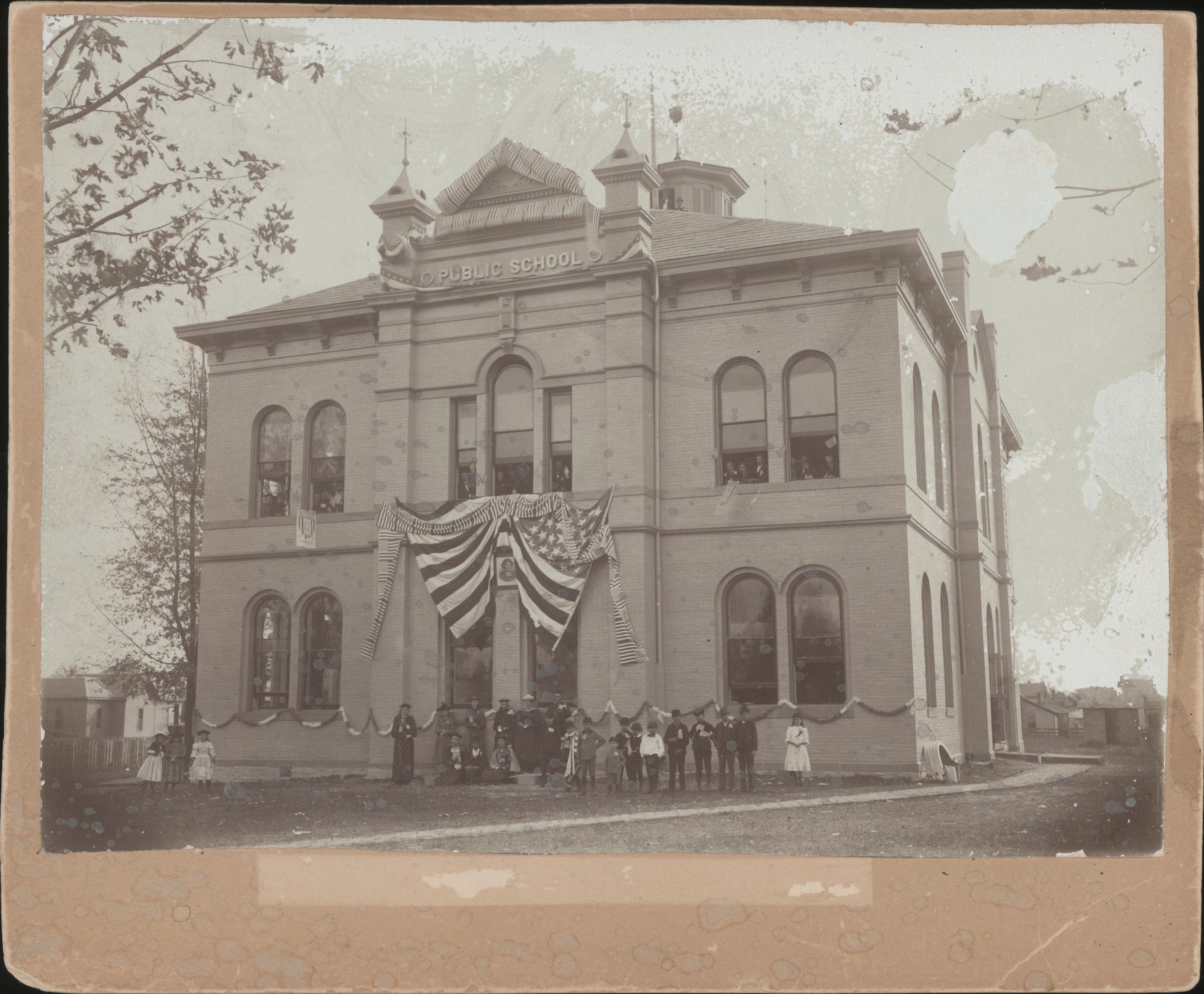 Tipton High School in 1869. An American flag adorns the front of the building. Group of people standing in front of the doors