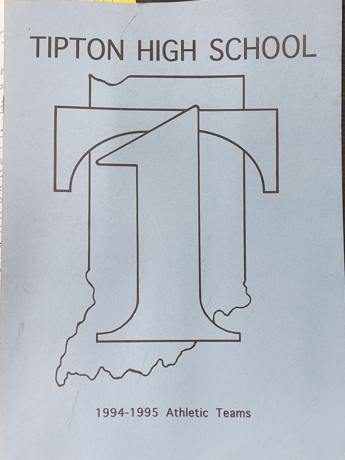 Scan of the front of a THS Athletics Teams book. Has an outline of Indiana, and a T is formed with the number 1.