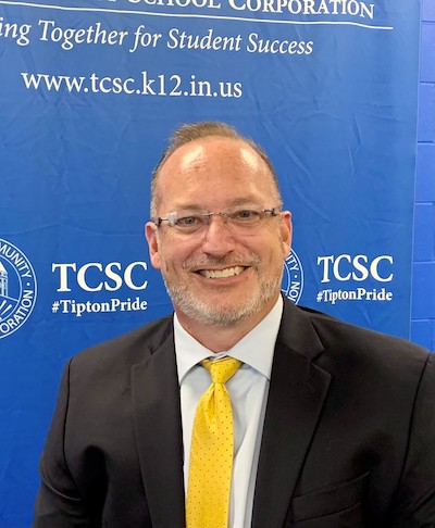 Ryan Glaze, superintendent, stands in front of a blue and white TCSC backdrop.