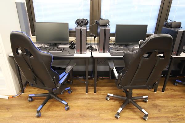 Two PCs, chairs, and monitors are together, yet a bit separated from the rest of the room