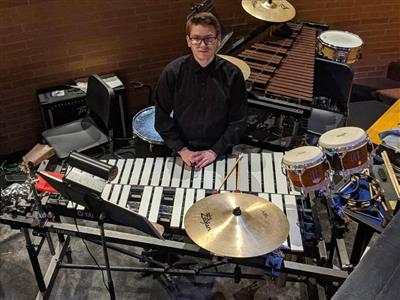 Student Zach Peters, expression serious, sits, surrounded by instruments.