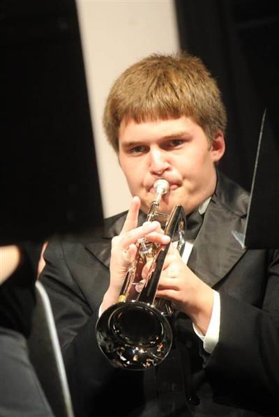 Student Mason Henderson plays a trumpet during a concert. He has light brown hair and wears a black suit.