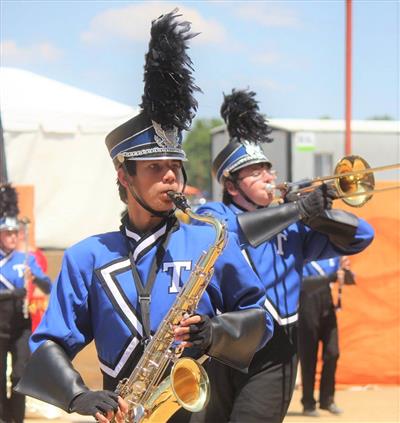 Band members performing. They wear a more traditional band uniform featuring black pants and a blue jacket with a white T on it.