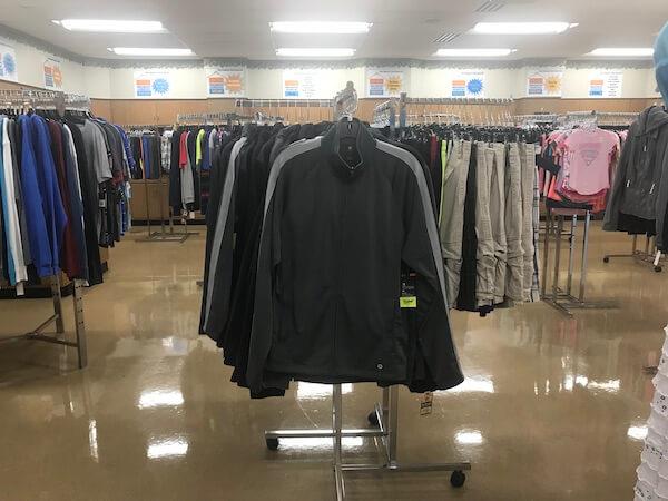 View of the clothing racks for teenaged boys. We can see a black zipup hoodie and other racks