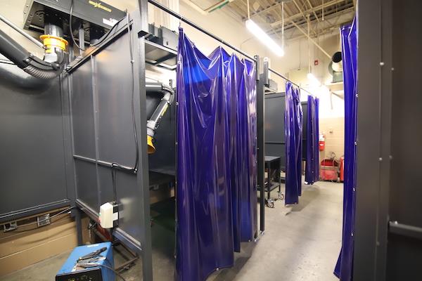 A photo of a row of welding booths. All booths have the protective plastic door coverings.