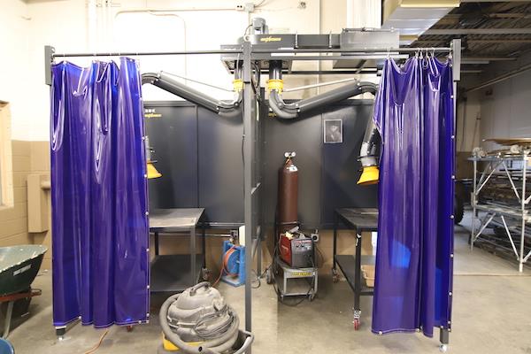 Two welding 'booths' are shown; a safety blue plastic curtain hangs in the doorways.
