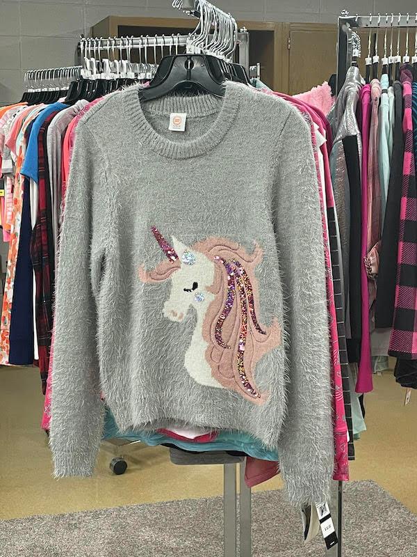 cute gray sweater featuring a unicorn on the front hanging on a rack
